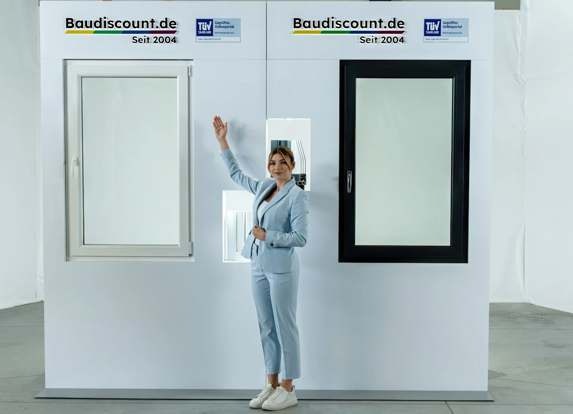 In blauer Jacke zeigt die Frau zwei Arten von Kunststofffenstern und deutet auf eines davon.