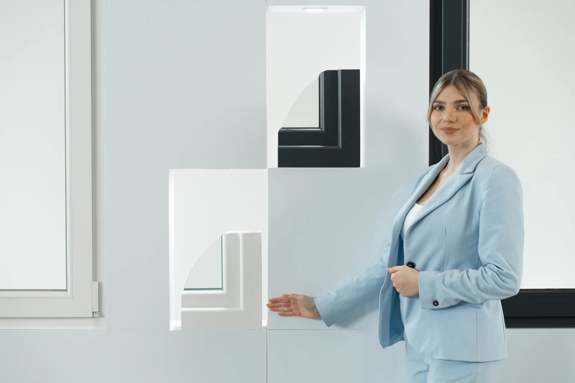 Frau in einem blauen Blazer, die zwei Arten von Fensterprofilen präsentiert.